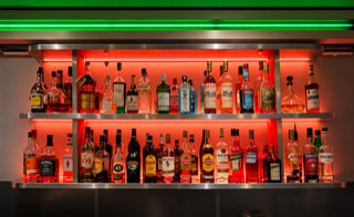Regal mit verschiedenen Flaschen Alkohol, rot beleuchtet, mit grünem Licht darüber.